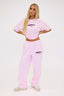 Person wearing a pink joggers and tee with burgundy dés vu logo on a white background