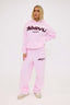 Person wearing a pink tracksuit with burgundy dés vu logo on a white background