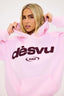 Person wearing a pink hoodie with burgundy dés vu logo on a white background