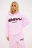 Person wearing a pink tracksuit with burgundy dés vu logo on a white background