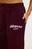 Close up of burgundy hoodie with dés vu logo in pink on a white background