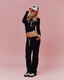 A woman wearing a navy cropped long-sleeve top and matching navy sweatpants with yellow drawstrings set against a solid pink studio background.