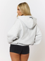 Woman wearing grey hoodie on a white background.
