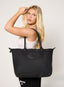 Woman holding a black tote bag against a plain background
