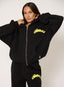 Woman wearing black waffle tracksuit with citron yellow branding on a white background.