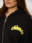 Close up of woman wearing black waffle zip up with 'desvu' citron yellow logo.