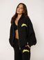Woman wearing unzipped black waffle tracksuit with citron yellow branding on a white background.