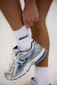 Person wearing a white sock with 'desvu' branding and a blue and gray athletic shoe.