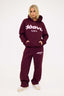 Person wearing a burgundy tracksuit with  dés vu logo in pink on a white background