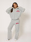 Woman wearing unzipped grey waffle tracksuit with coral 'desvu' branding on a white background.
