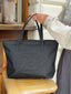 A person holds the top handle of a black tote bag with an embossed 422 oval logo on the front, set on a tan leather chair in an indoor setting.