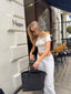 A woman wearing 422 stone baby tee and white pants stands in front of a white storefront, holding a black tote bag with an embossed 422 logo.