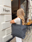 A woman carrying a black tote bag with embossed 422 logo detailing, standing outside a white storefront.