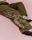 Olive green sweatpants with a large yellow script logo print, shown on a model wearing black and white sneakers against a solid pink background.