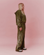 A woman stands in profile wearing an olive green matching lounge set with yellow abstract line-art graphics, set against a solid pink studio background.