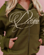 An olive green zip-up hoodie with a large yellow script graphic on the front, worn by a model with blonde hair against a solid pink background.