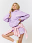 Woman wearing lilac hoodie and shorts with 'des vu' branding on a white background.