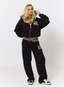 Woman wearing black tracksuit with teddy plaid print 'des vu' branding on a white background.