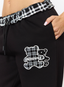 Closeup of woman wearing black joggers with teddy plaid print 'des vu' branding on a white background.