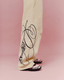 Yellow colored wide-leg sweatpants with a navy abstract graffiti-style line print on the lower leg, shown on a model wearing black and white sneakers against a solid pink background.